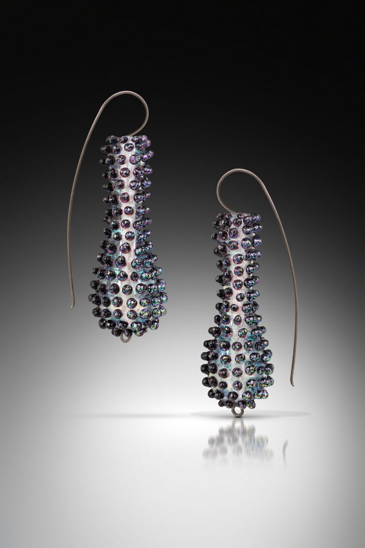Torch-formed dichroic glass  soda lime glass  oxidized sterling silver. The core shapes are made first using a graphite dowel &amp; gravity. The first basic shape goes into the kiln while I start the second. Once I match the two earring shapes  I add the outer texture in iridescent black dichroic glass.