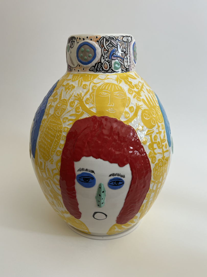 ceramic vase mainly decorated with white and yellow sgraffito, featuring a large human face with red hair and slightly raised green nose.