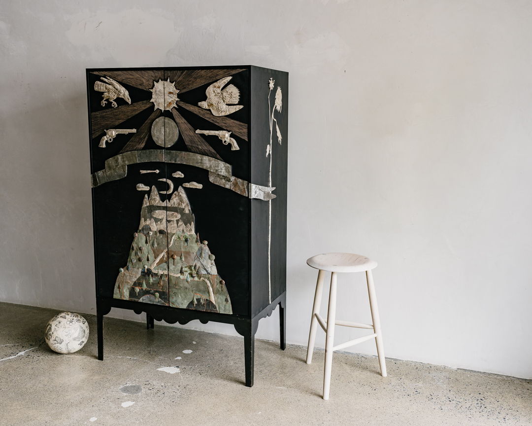 Rosehill Cabinet  Ebonized Walnut case Blackened Steel base birds of prey  mountain  revolvers  and sun motifs hammered silver sunflowers on sides hammered silver  reclaimed aluminum  oxidized copper  carved details wraparound sculptural banner with reclaimed aluminum