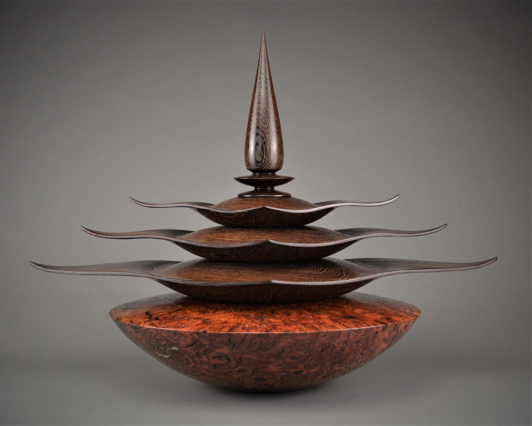 The Wenge finial lid fits upon three flowing hollowed out Wenge diamond boxes receding in size perfectly fitted to stack upon each other  which fit and set upon the large hollowed out Jarrah Burl storage vessel (base). Innovatively sculpted on the lathe at over 2000 rpm.