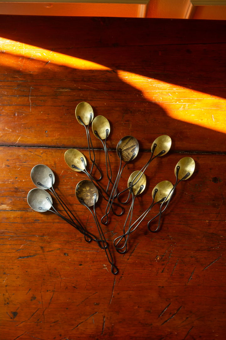 A grouping of Dessert and Foliage spoons  forged in brass with blackened stainless steel handles. The Foliage spoons are shown with Fern and Burberry motifs in tinned and antique brass. The Dessert spoons are shown in raw brass.