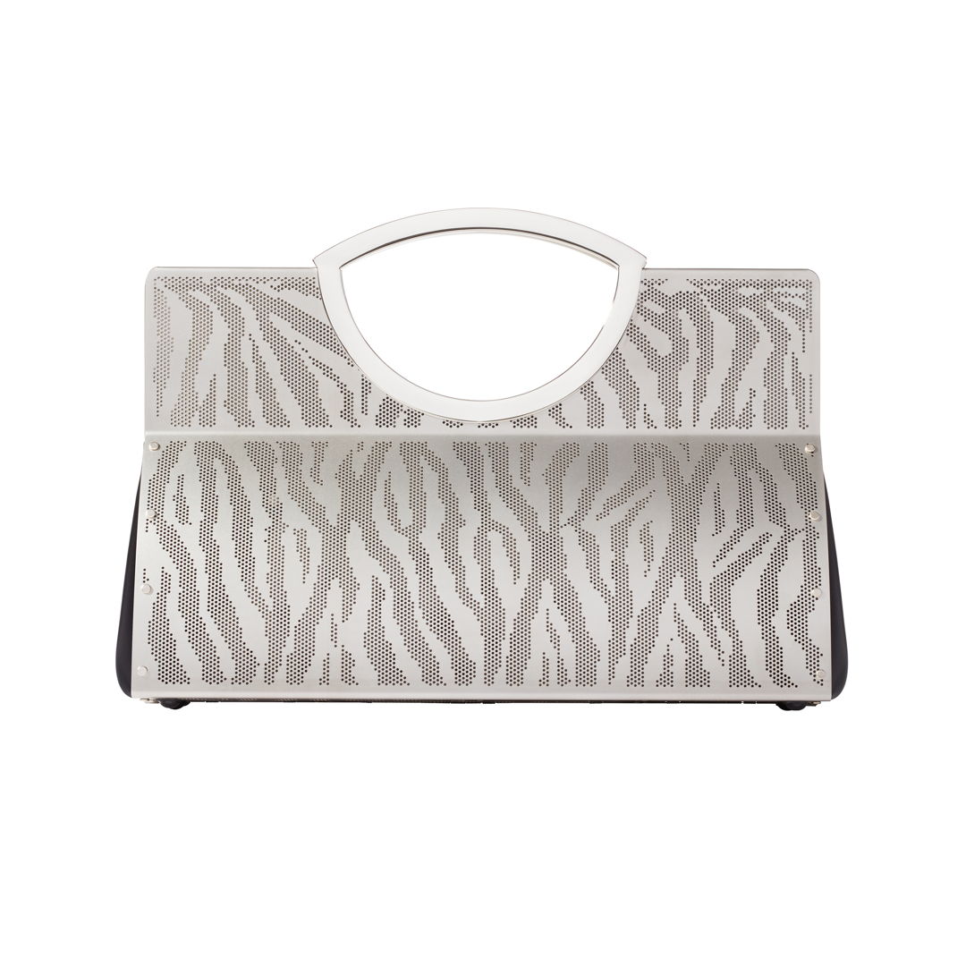 The zebra tote is hand fabricated in etched stainless steel with leather gussets  double handles and a spring hinge closure.
