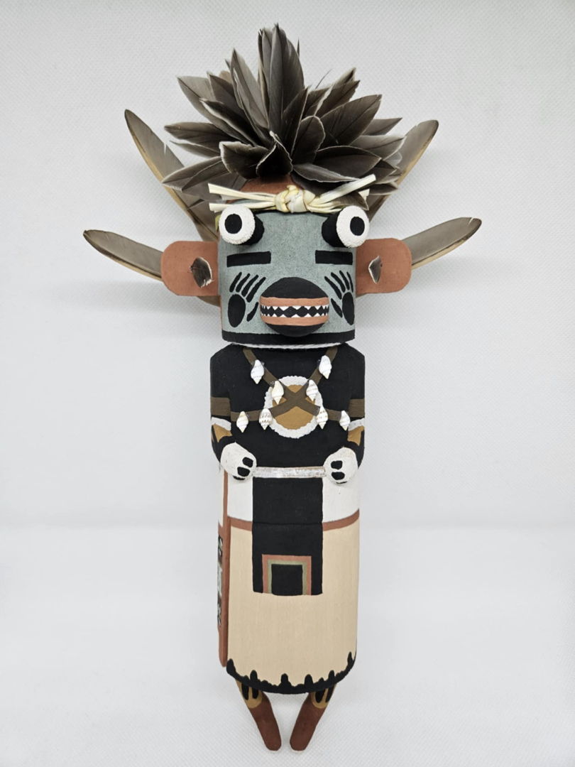 The Blue Badger Kachina is one of many badger kachinas that appear on Hopi during the winter and summer months  he is a symbol of strength  healing and protection. The blue badger is carved out of dried aged cottonwood root  painted with natural earth mineral paints that I hand collect and process myself. Duck feathers  quail feathers and shells are used to complete the blue badger kachina.