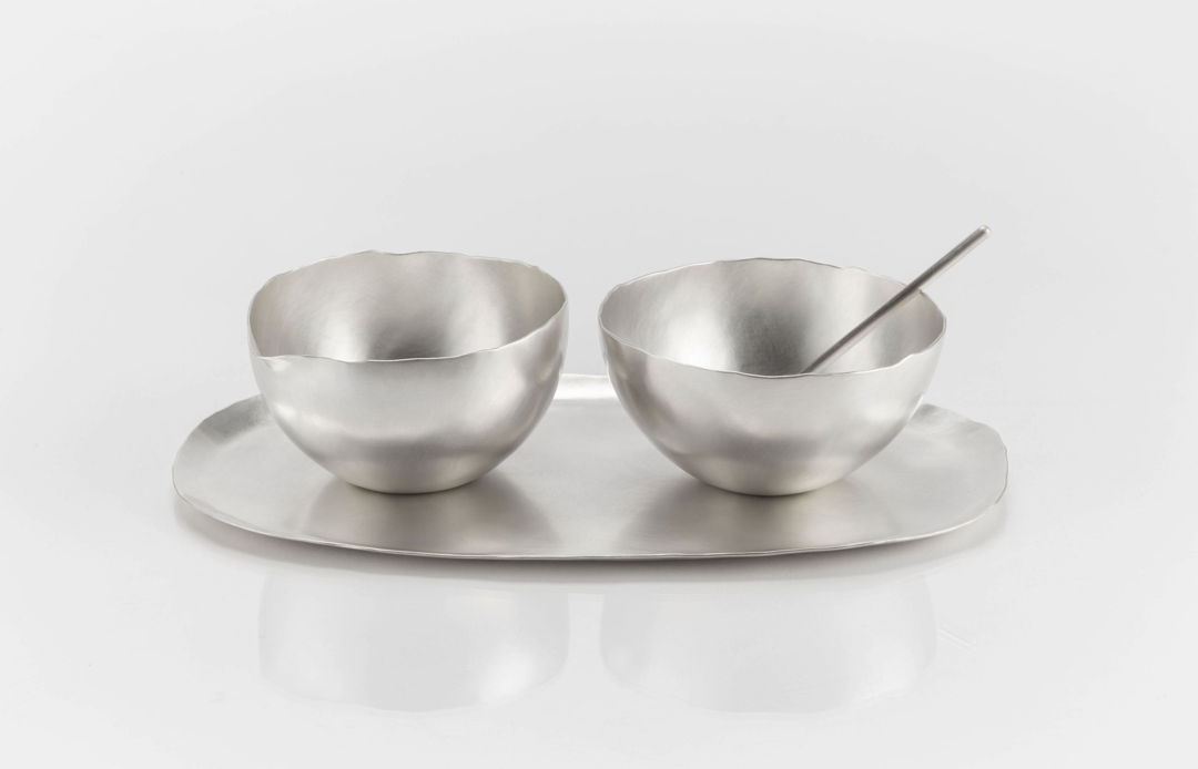 A sugar  creamer  tray  and spoon set. The creamer has a subtle spout included in the form. The vessels and trays were made from hammering flat sheets of silver up into three dimensional forms.