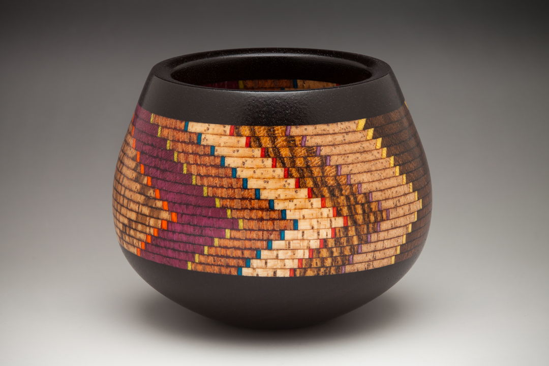 This small ceremonial bowl has 10 specie of wood and artist dyed maple veneer. there are 400 individual pieces of wood in it  with an Ebony base and rim. The shape of the bowl echoes the pattern of the lamination which reminds me of the Anasazi bowls