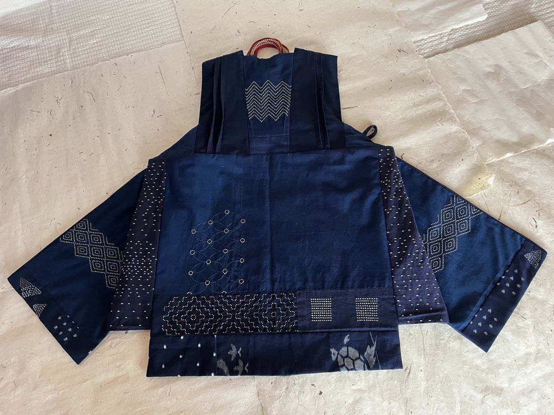 This piece is the result of an experiment to transform indigo-dyed  cotton fabric into a creative image that mirrors the shapes and three-dimensional structure of origami. The various shades of indigo are decorated with stitches sourced from plant-based dyed thread.