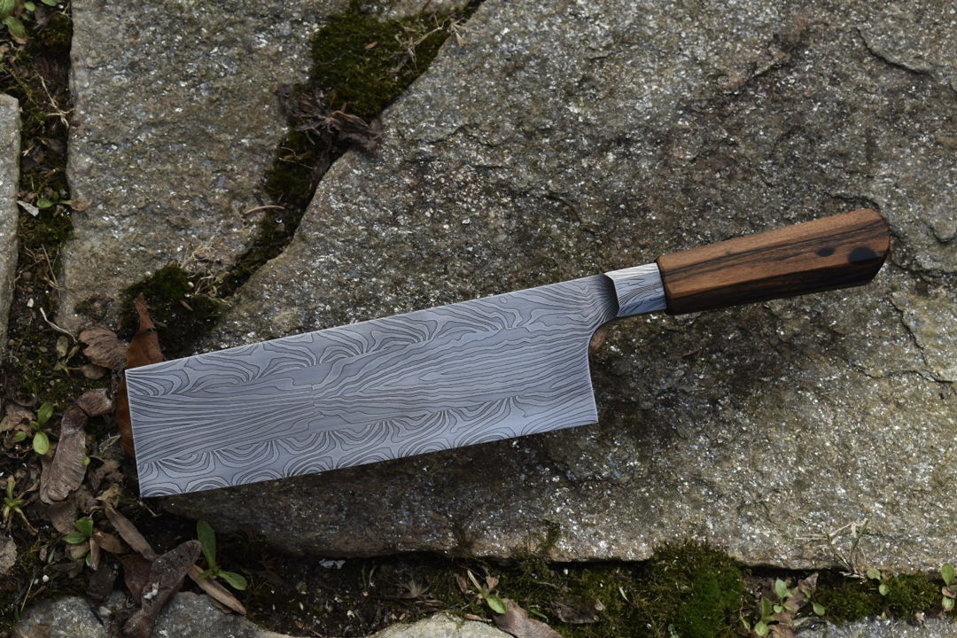 8" Nakiri with mosaic damascus blade. Handle is Black and White Ebony. The pattern is made by stacking alternating pieces of two alloys of carbon steel  then forge welding them together  basically melting the layers together into one piece. this is then restacked and manipulated to form a pattern of our choosing.