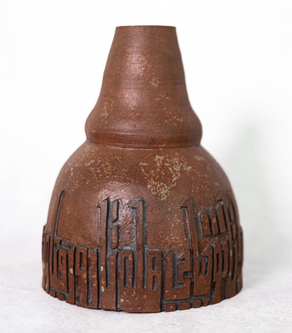 Brown vase with rough textured glaze and inscription along the bottom