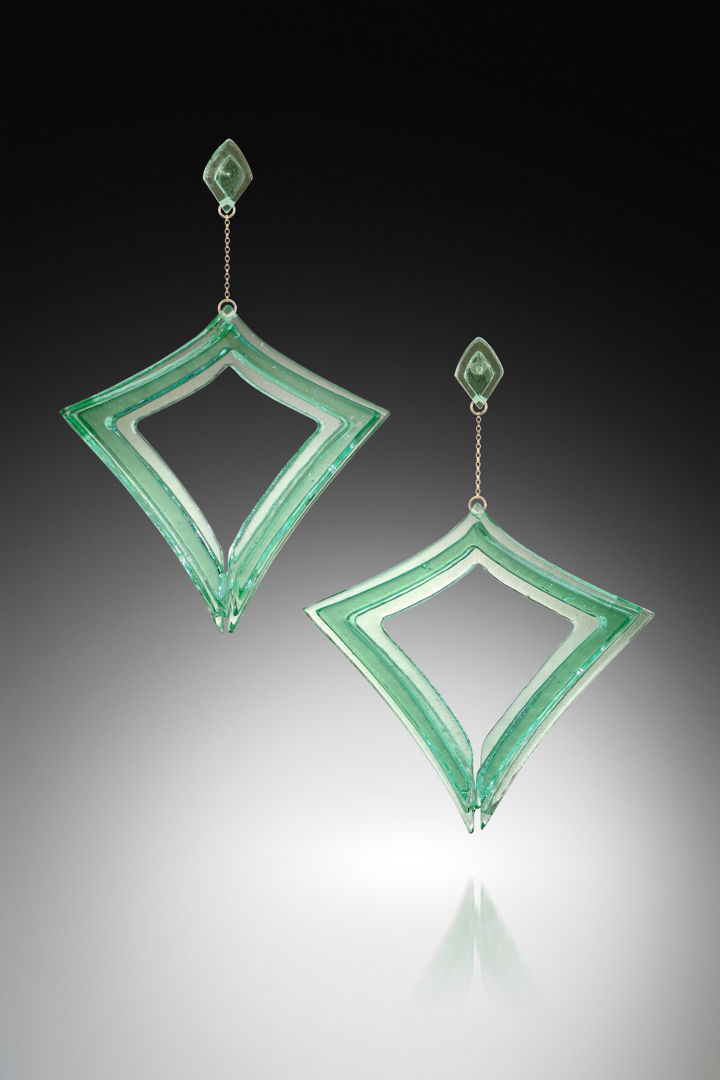 Digitally designed  waterjet cut glass  coldworked  polished  fused and laminated together to form two 3-dimensional glass forms. Sterling Silver posts are embedded into one while the second is suspended from a gold fill chain.