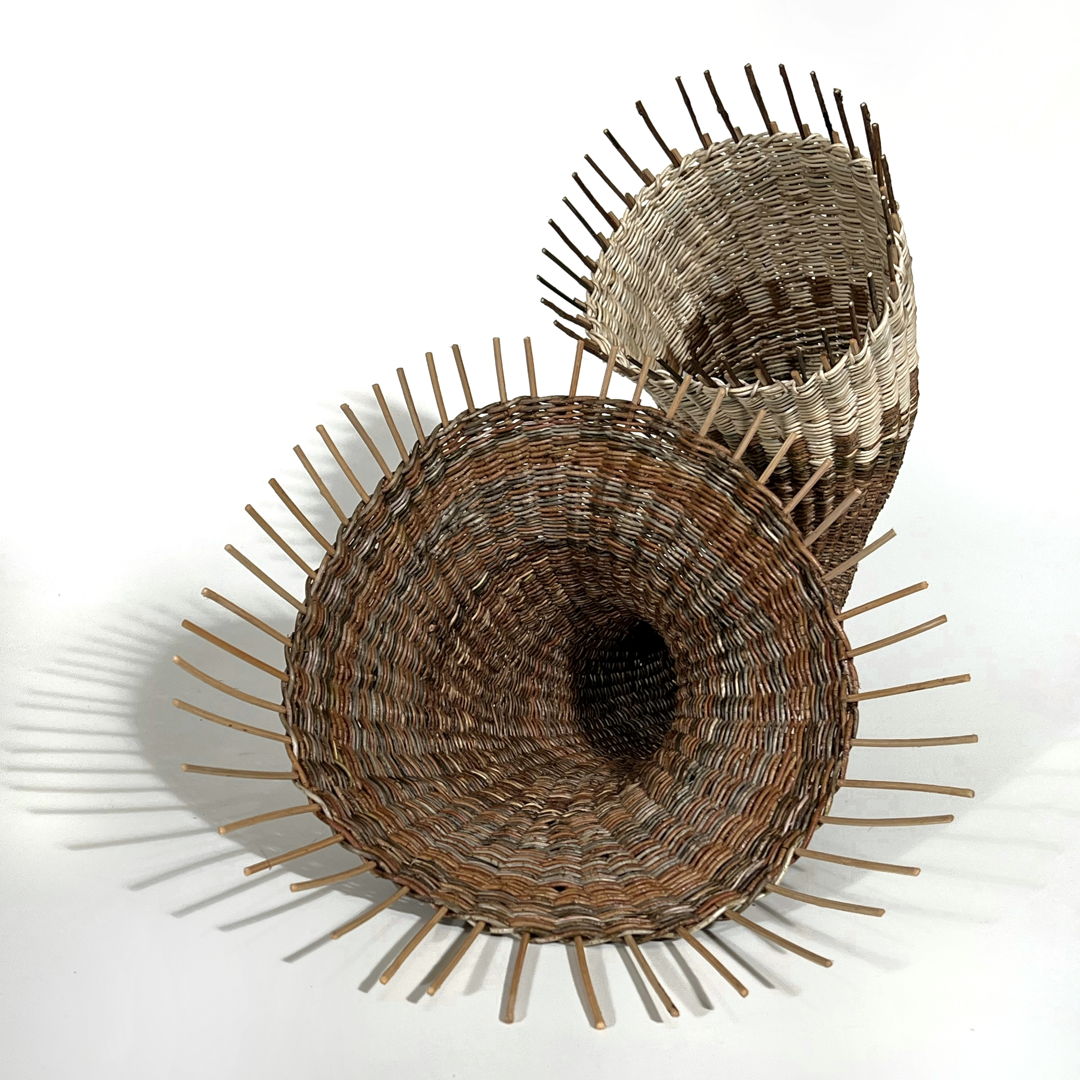 Rattan basket shaped like a horn with two open ends in  white, brown and gold tones.
