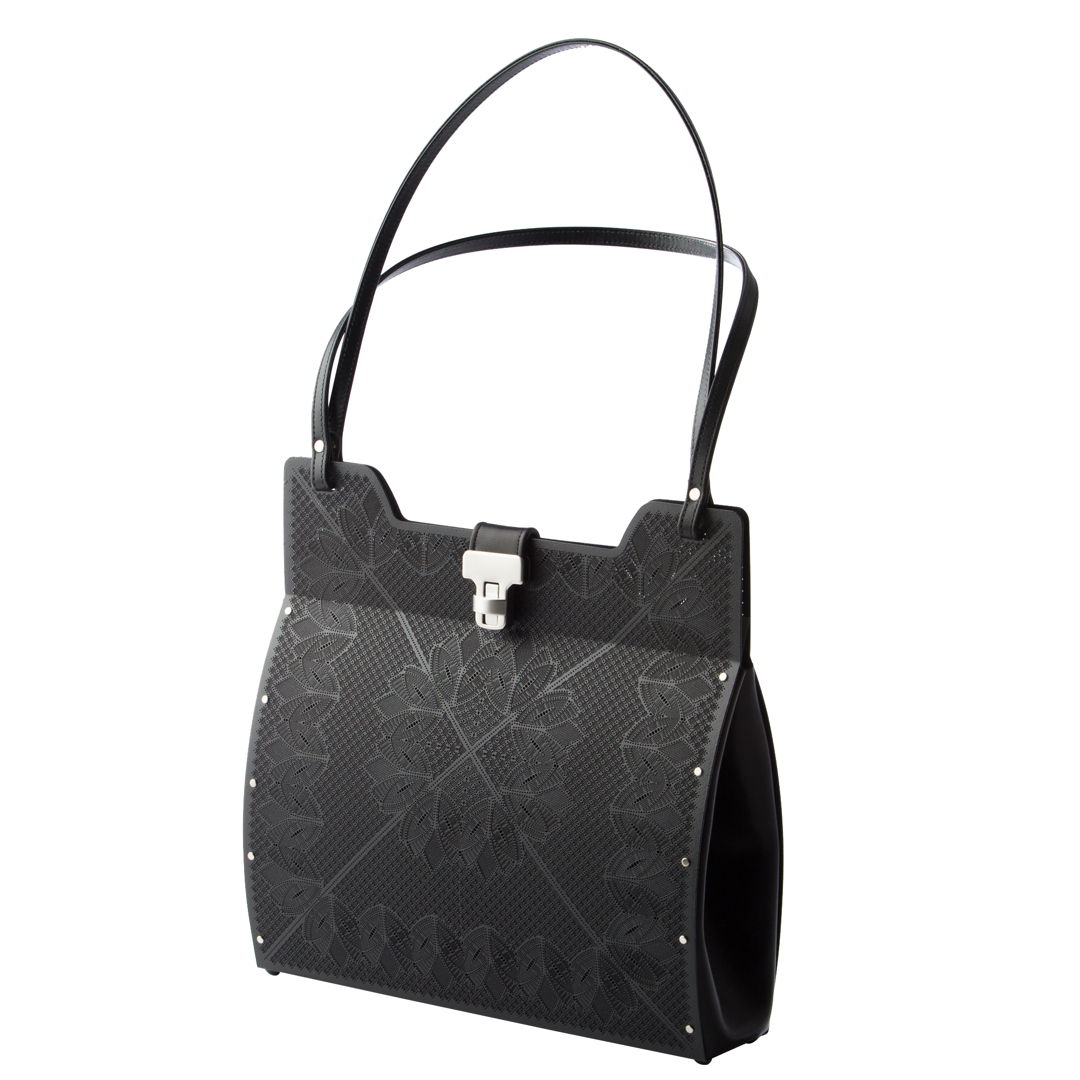 The lotus bag is shown here in the black finish and is hand fabricated in stainless steel with black leather gussets  double shoulder straps and a turn lock closure.