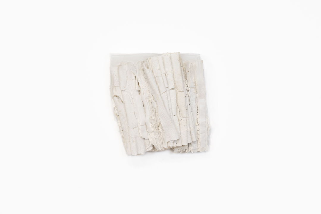 Porcelain sheets are folded and compressed  then packed with white clay between the layers. A light wax accent softens the surface and seals the fragile edges  preserving the fine textures. The piece reads like a small bundle of pages or strata—a quiet study in touch  fragility  and time.