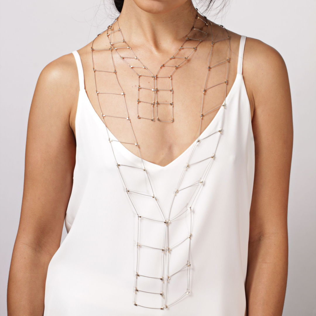 Two neckpieces layered to create a geometric  tapestry-like neckpiece in soft  woven stainless steel cable finished with 14k gold fill hardware. The pieces fold on themselves and can be crushed but still retain their shape and linear form.