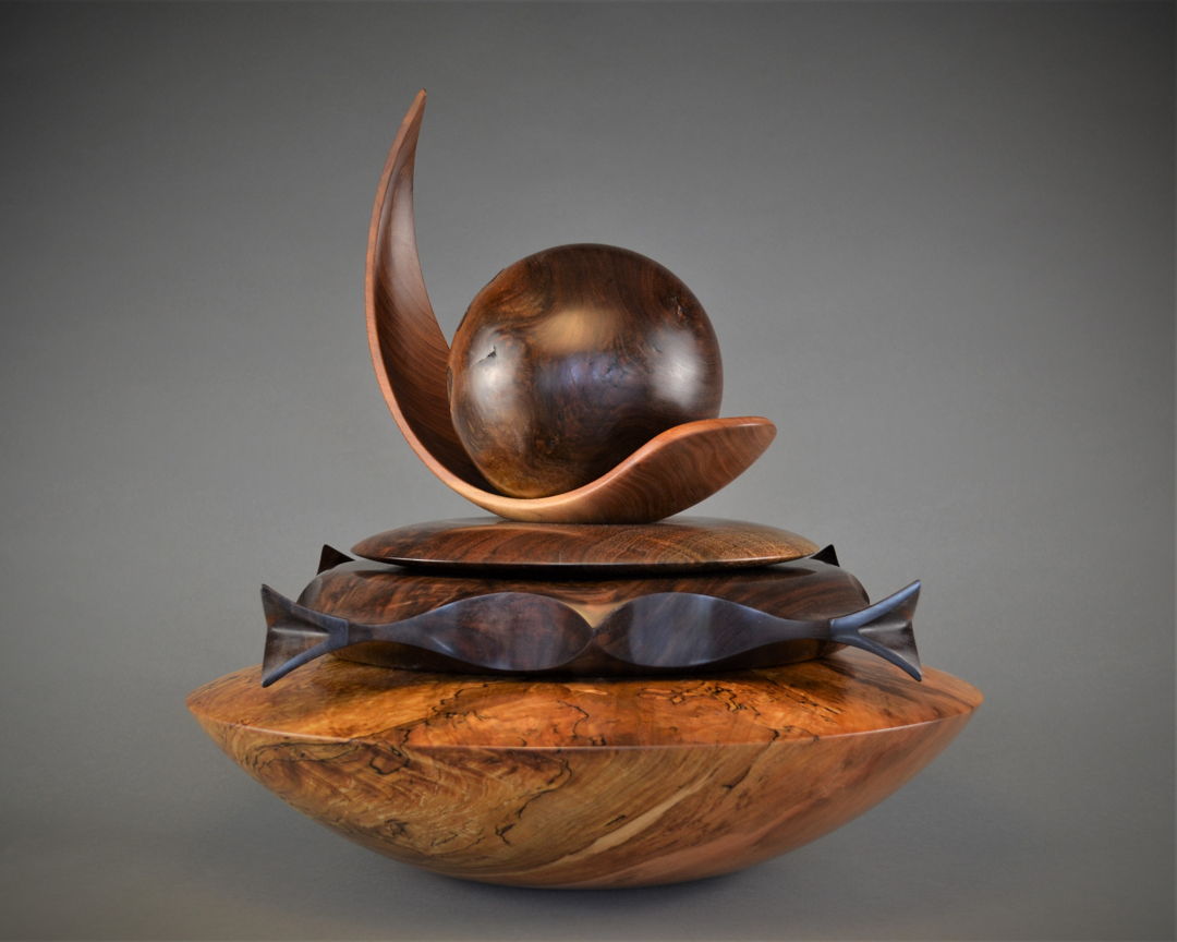 Black Walnut Burl Sphere (luna) rests upon the concave talon shaped Cherry swoosh and Black Walnut Disc. The ornate Black Walnut form features 2 kissing fish on each side and singing bird-heads on each corner which fits upon the large Spalted Maple hollowed out storage Vessel (base).