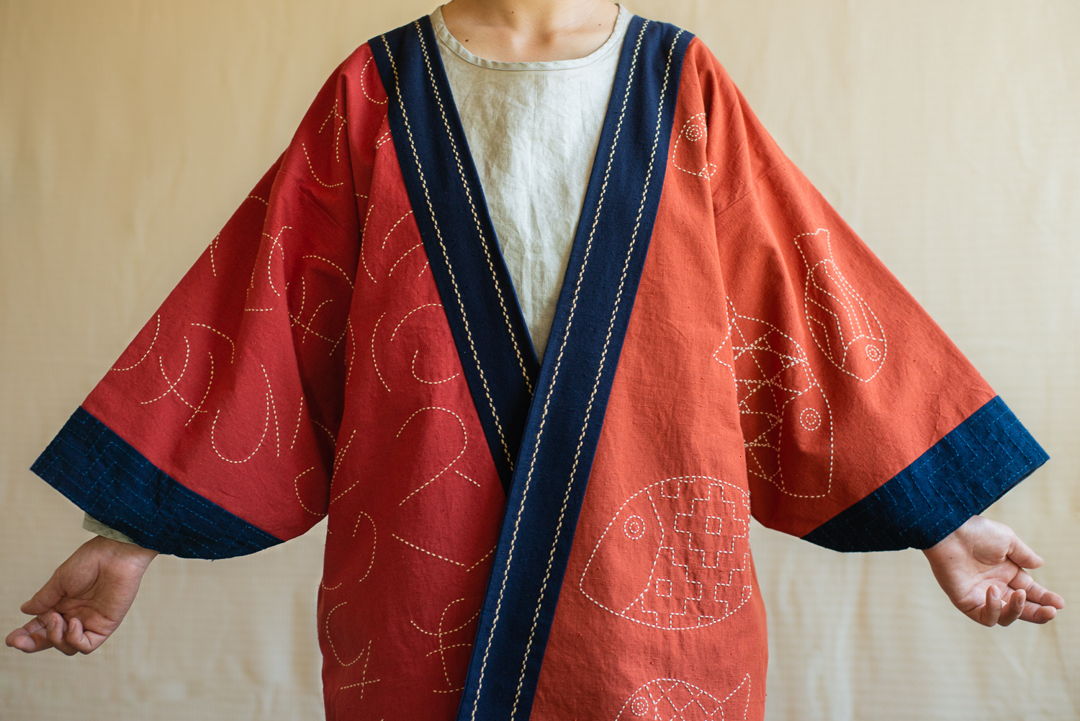 The jacket is hand-stitched on cotton fabric dyed with madder and indigo. The poem stitched on the piece signifies that each end exists solely because of a beginning. The fish bring the philosophical message to life by symbolizing the vivacious cycle of life on Earth.