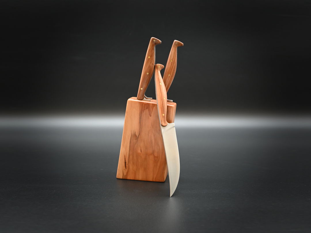 Set of four steak knives  with carbon steel blades and applewood grips  mounted in an applewood block. The assymetrical rivets and slender grips draw inspiration from artifaces in the London Museum's late medieval tableware collection.