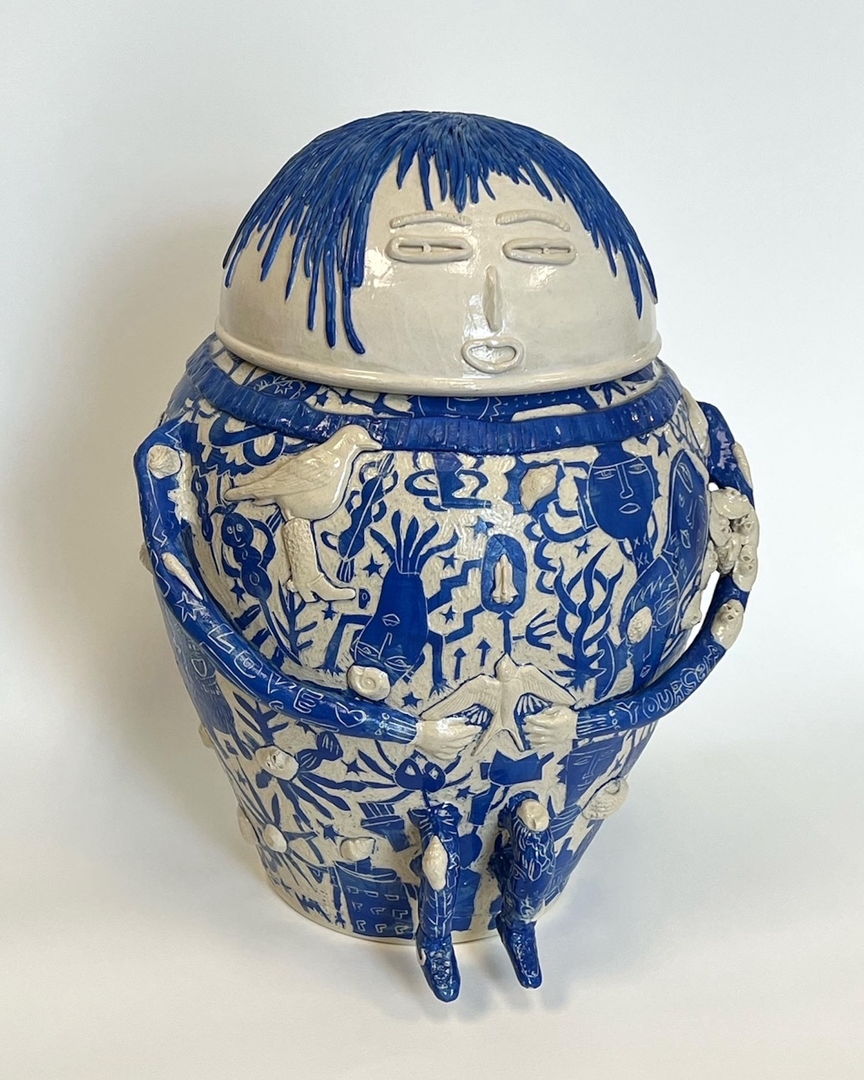 White stoneware sculpture of a sitting human figure covered in bold blue graphic illustrations.