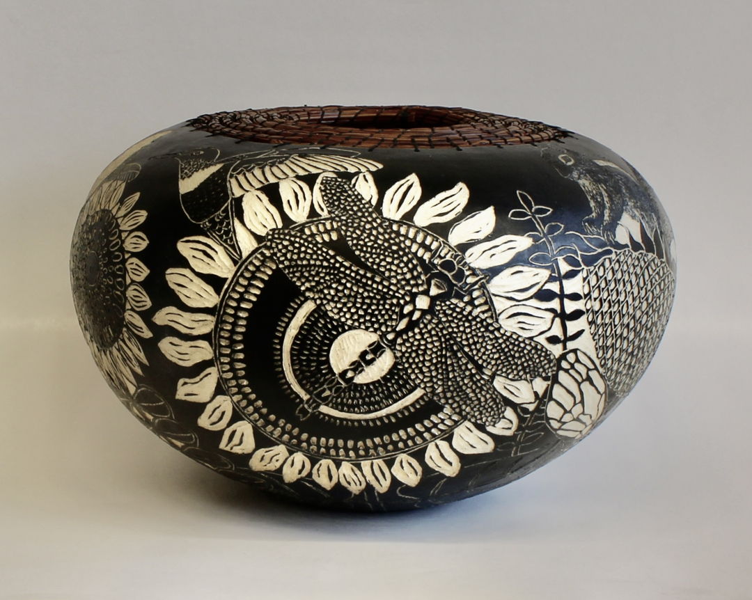 The images on the surface of the pot were created using sgraffito and depict flowers  insects  birds and a chipmunk. The top is edged with woven pine needles.
