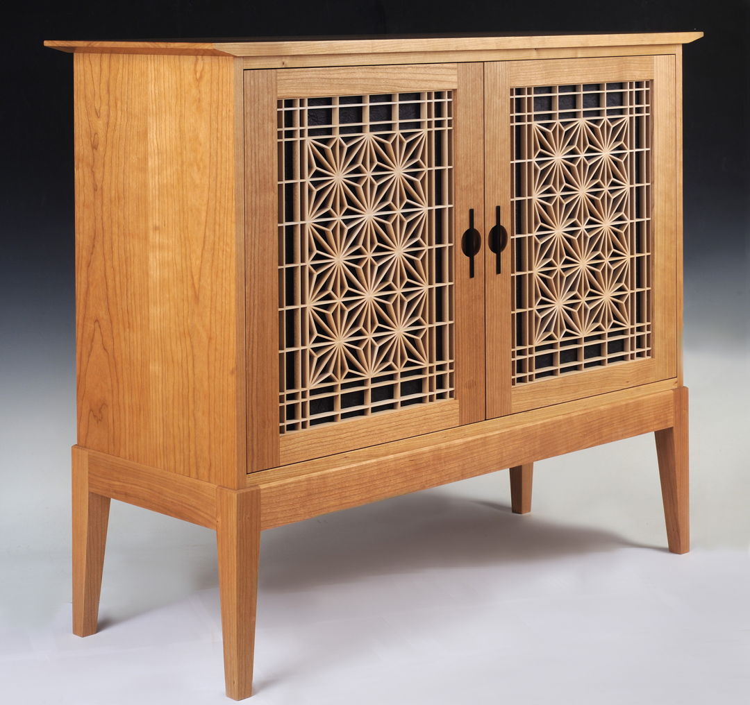 Shaker and Japanese inspired solid cherry cabinet featuring the asa-no-ha (hemp leaf) kumiko pattern backed by black crinkled Japanese momigami paper in the doors. The door pulls are ebonized cherry. The interior features a solid wood adjustable shelf. The back is frame and panel construction.