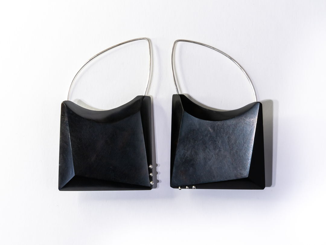 Hand Shaped and polished African Black Wood with Argentium Silver details and ear wires. A locking system is employed to bond the metal and wood. A keyhole system is drilled within the wood and the metal is knurled before epoxying wood and metal together.