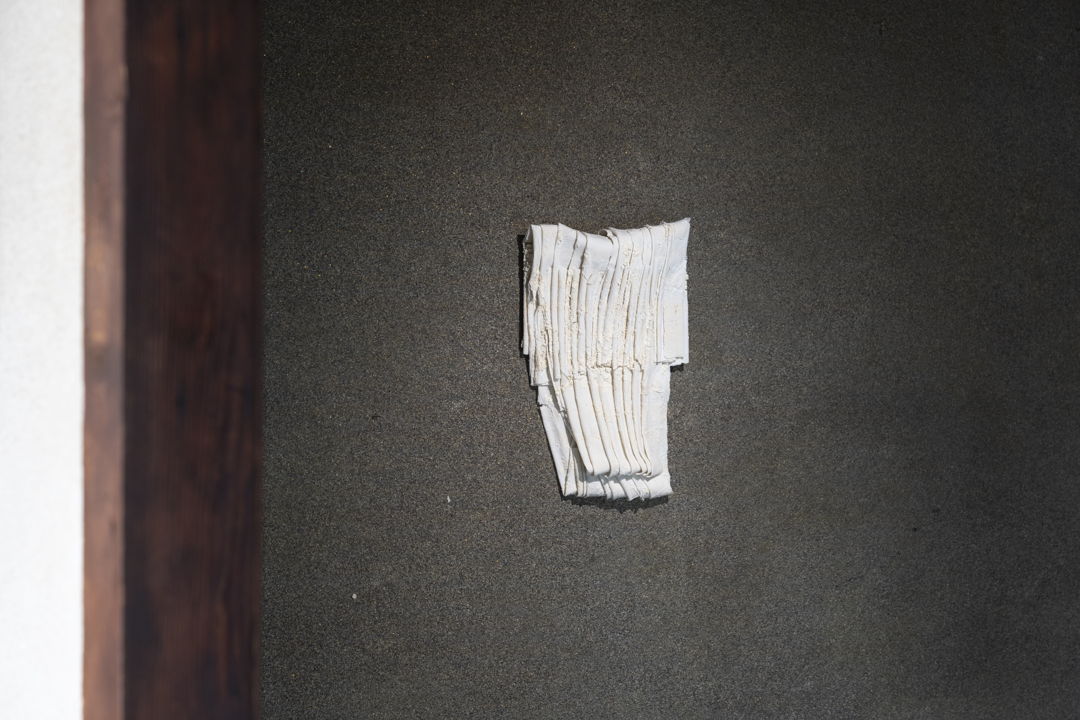 Porcelain sheets are folded and compressed  with white clay powder packed between the layers before firing. The powder settles into the seams and creases  preserving a fragile  papery texture and soft drift of sediment. The piece reads like a small bundle of pages—a quiet study of touch  erosion  and care.