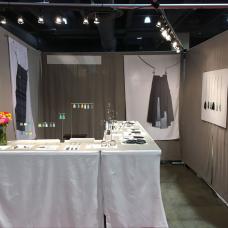 Booth with tables with white table clothes in an L shape showing the jewelry