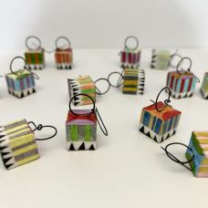 Circus Earrings are lightweight  cube-shaped earrings. Their dangle is made from annealed steel wire hammered and shaped into circles. The cubes are hollow and made from mat board  with layers of assorted colorful papers “painted” on with brush and glue. The same process is used for the colorful and detailed patterns. All paper jewelry is sealed for wear.