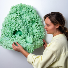 A woman stands to the left of a green glasswork art installation