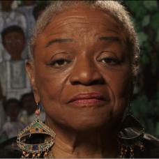 African American female with short hair and decorative earrings is looking straight at the camera