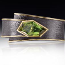 Cyclone wrap cuff in 18k gold and oxidized sterling silver  bezel set with 16.6 carat of faceted green tourmaline. A two part  hinged cuff with a flat spring  the cuff wraps around the wrist and closes with a snap.