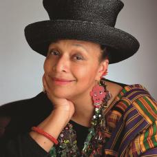 African American female wearing a black hat with a colorful earring, necklace and wrap