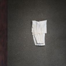 Porcelain sheets are folded and compressed  with white clay powder packed between the layers before firing. The powder settles into the seams and creases  preserving a fragile  papery texture and soft drift of sediment. The piece reads like a small bundle of pages—a quiet study of touch  erosion  and care.